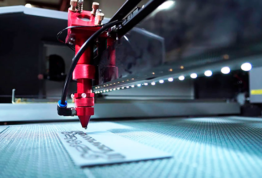 Primer plano del cabezal de una máquina de marcado láser, marcando una plancha de plástico.